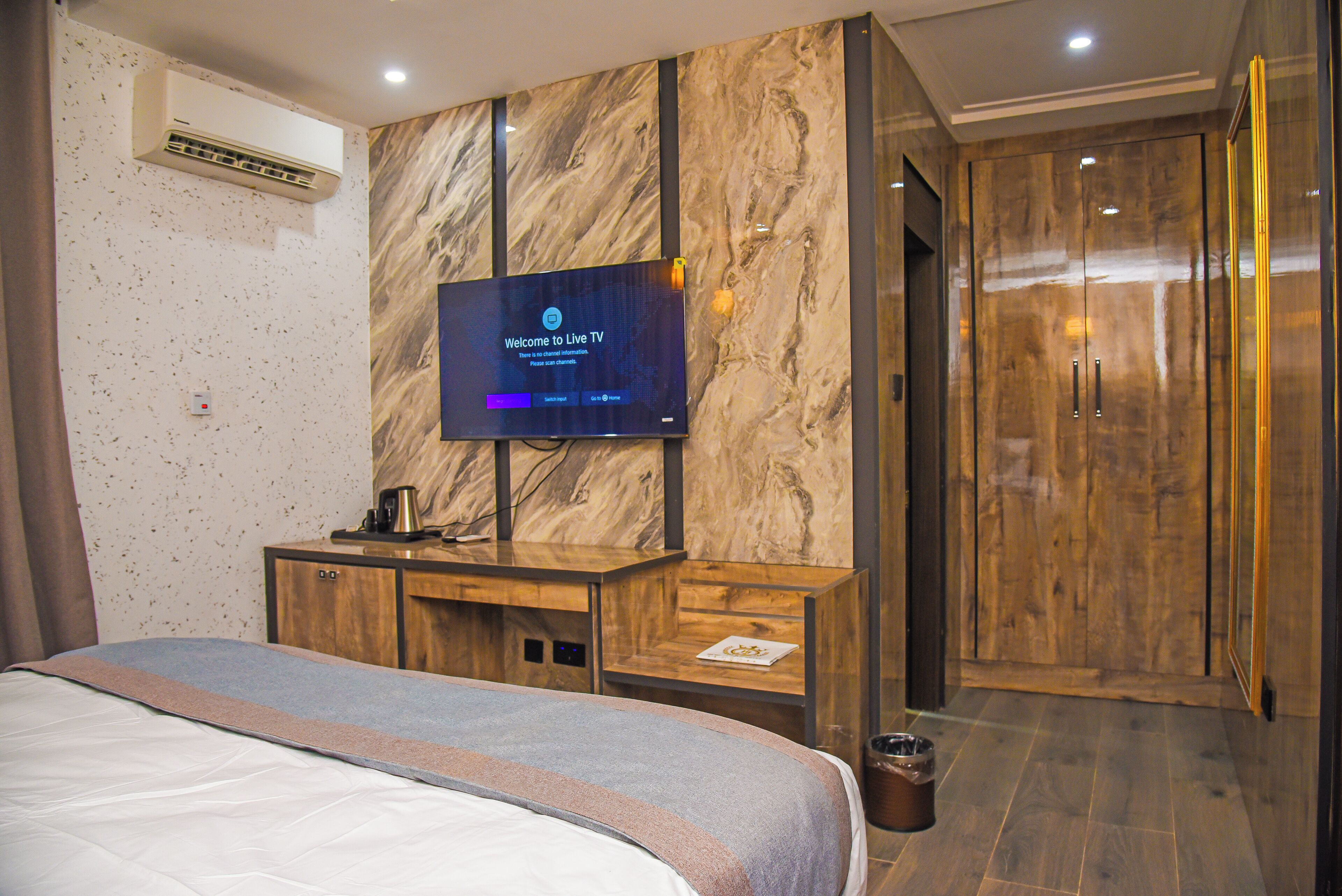 Ein Hotelzimmer mit einem Bett, einem an einer Marmorwand montierten Fernseher, einem Holzschrank und einem Kleiderschrank.