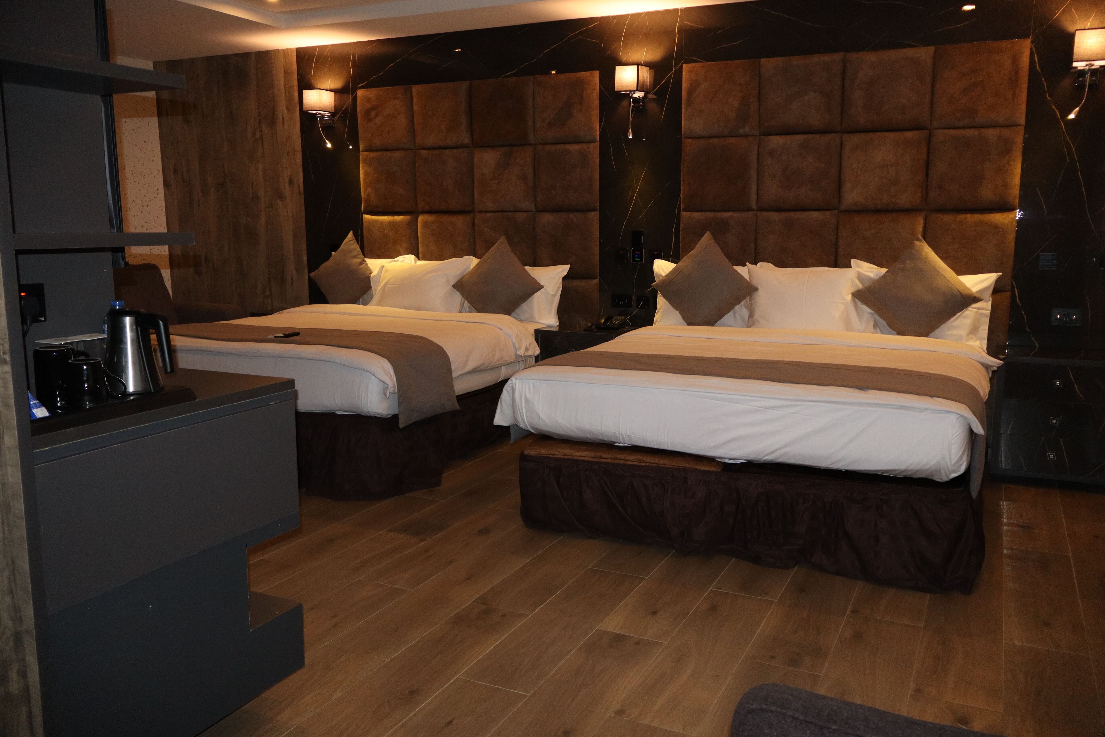 A hotel room with two beds, wooden flooring, and a modern headboard design.