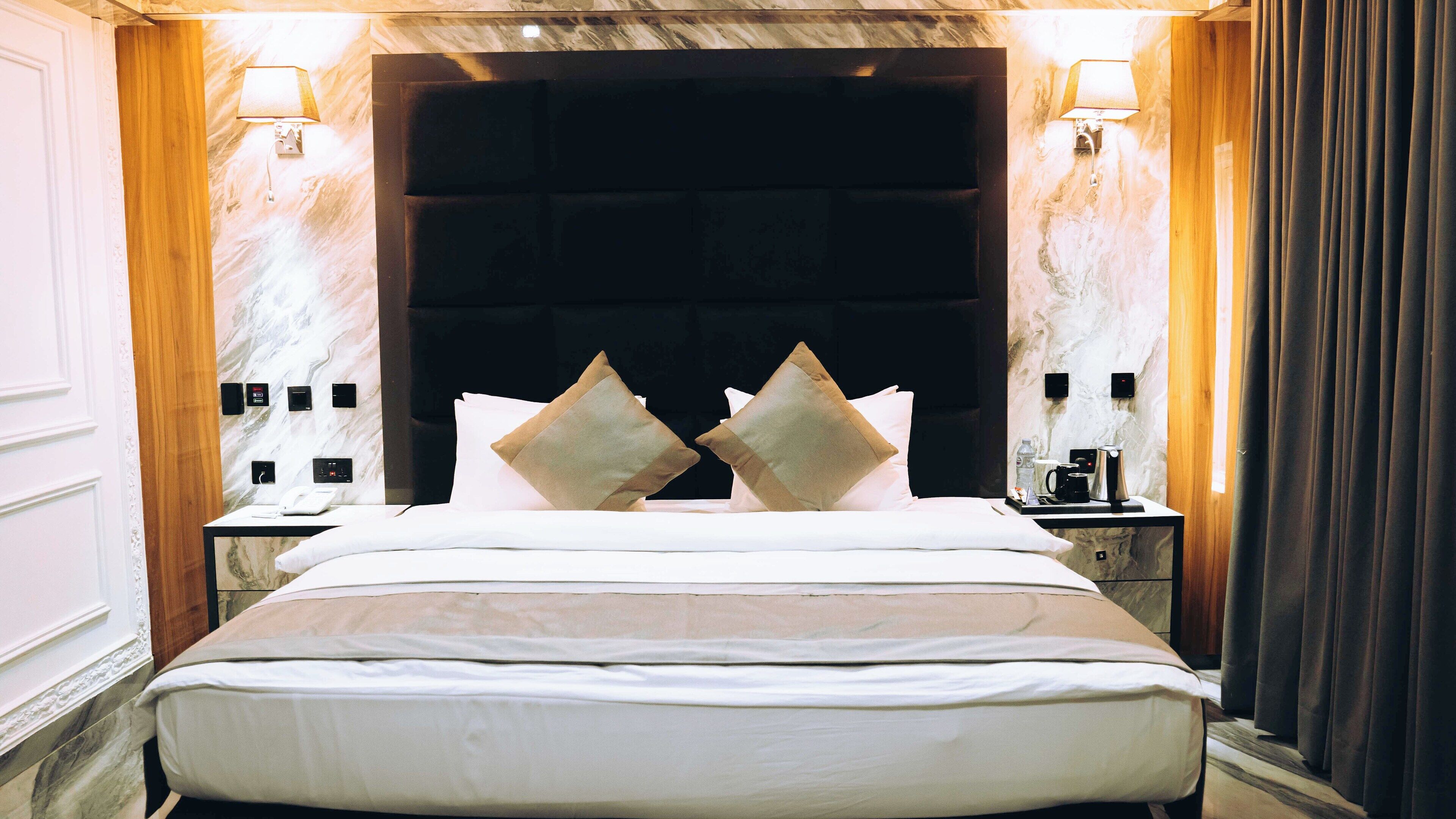 A hotel room with a large bed, two bedside tables, a headboard, and wall-mounted lamps.