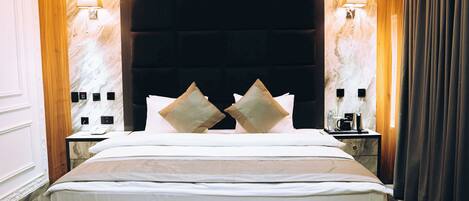 A hotel room with a large bed, two bedside tables, a headboard, and wall-mounted lamps.