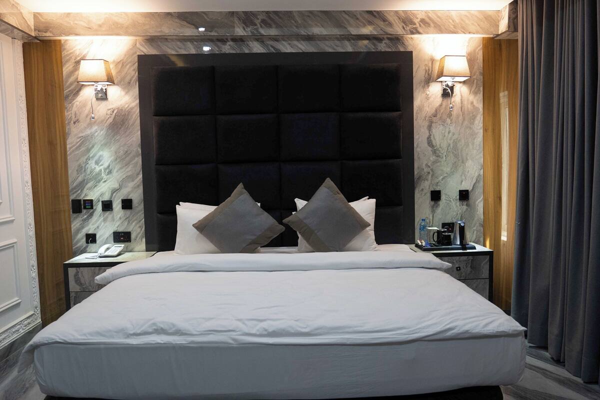 A modern hotel room with a large bed, two bedside tables, a marble wall, and a dark headboard.