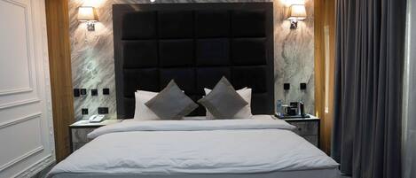 A modern hotel room with a large bed, two bedside tables, a marble wall, and a dark headboard.
