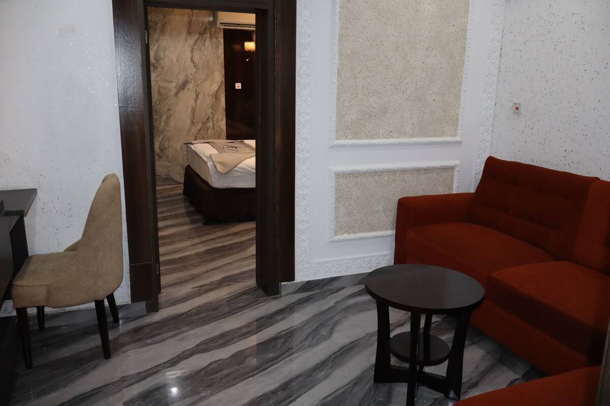 A modern hotel room with a marble floor, a red sofa, a beige armchair, and a small round table.