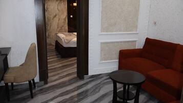 Una habitación de hotel moderna con suelo de mármol, un sofá rojo, un sillón beige y una pequeña mesa redonda.