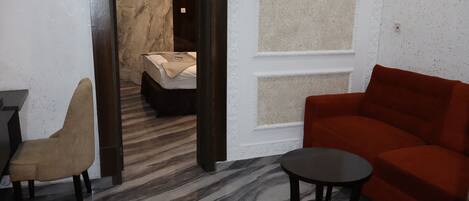 A modern hotel room with a marble floor, a red sofa, a beige armchair, and a small round table.