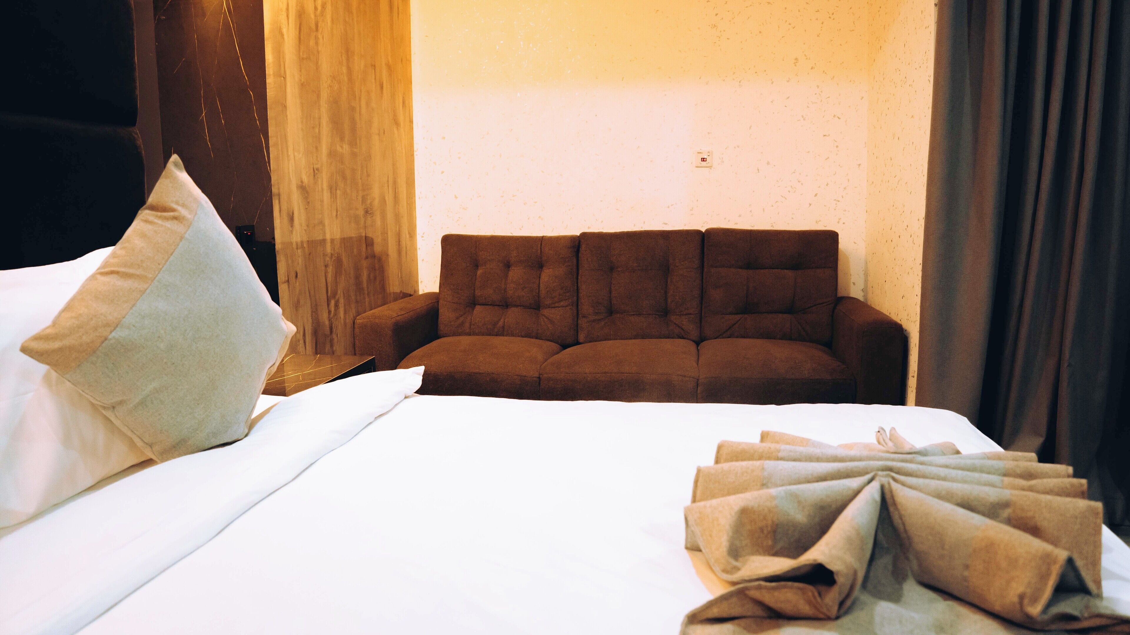 A hotel room with a large bed, a brown sofa, and a white pillow.