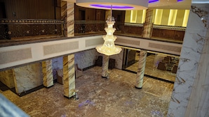 A grand lobby with a central chandelier, marble columns, and a high ceiling with recessed lighting.
