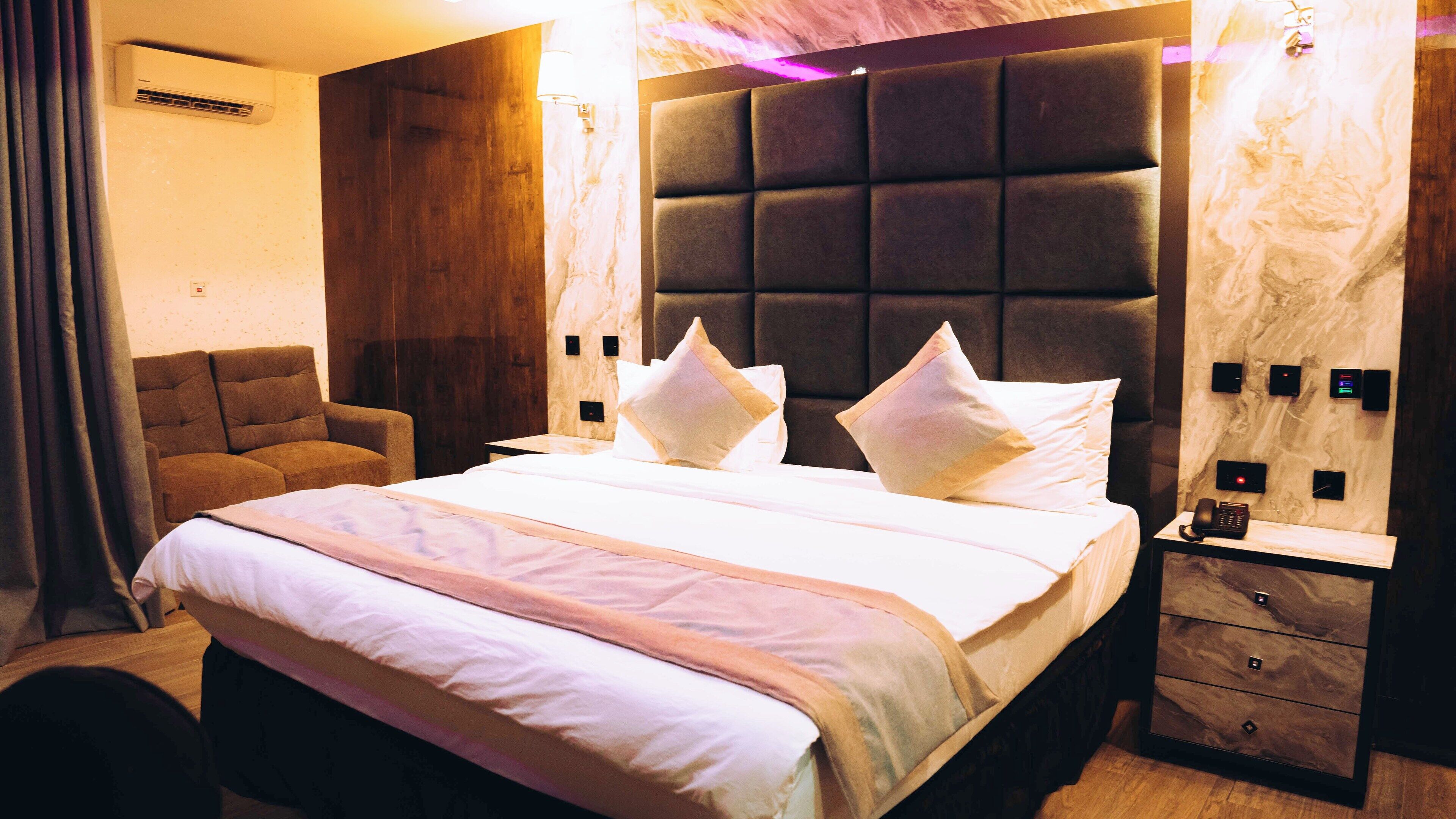 A hotel room with a large bed, a headboard with a padded back, a bedside table with a phone, and a nightstand with drawers.