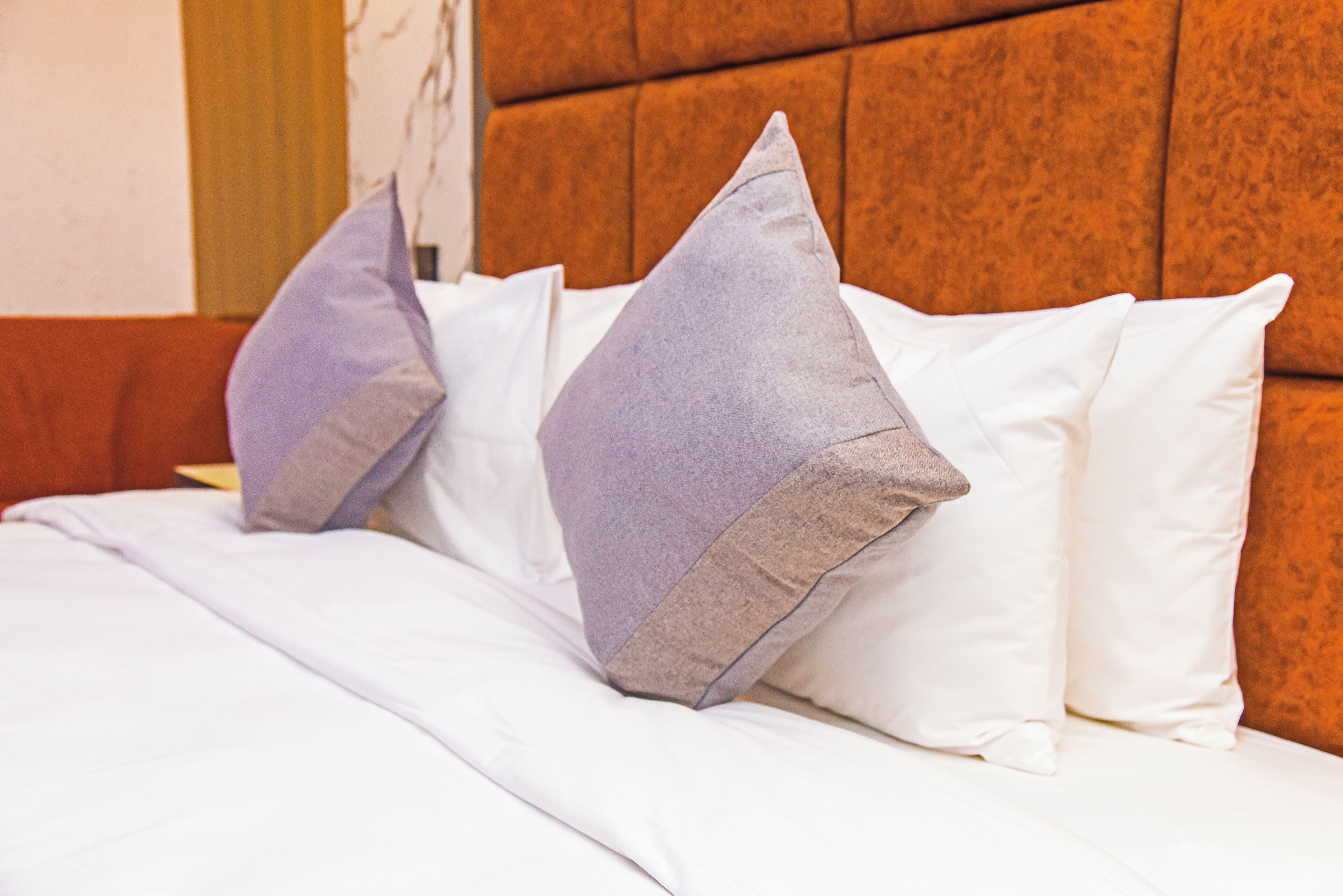 Ein Bett mit weißer Bettwäsche und zwei Kissen, eines grau und eines beige, an einem hölzernen Kopfteil.