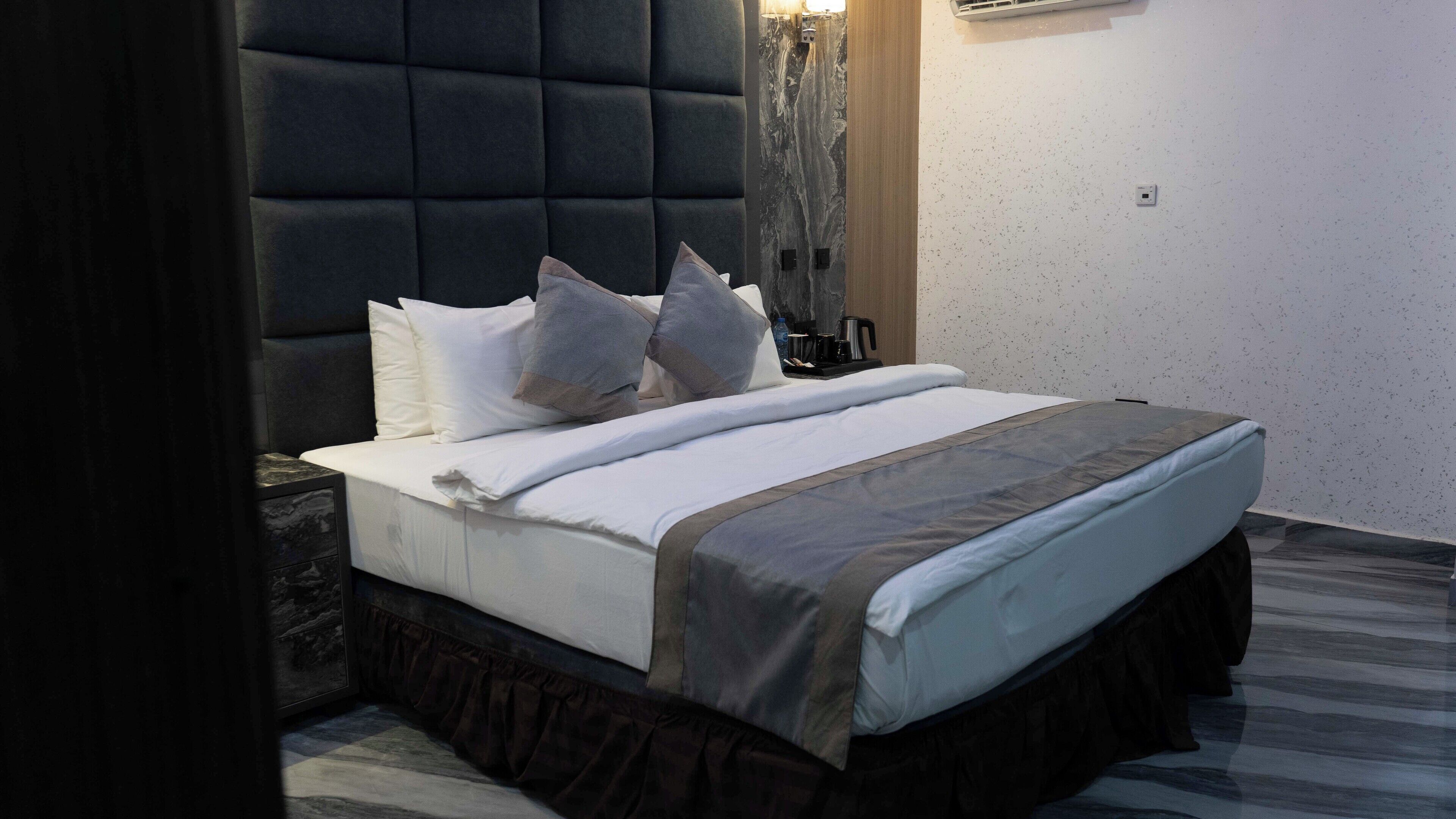 Een net opgemaakt bed met een donker hoofdbord, wit beddengoed en een grijze accentkleur.