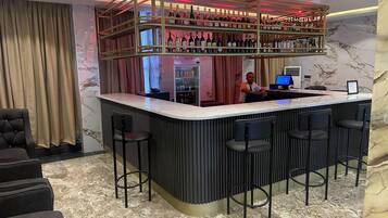 A bar area with a marble floor, multiple bar stools, and a bartender.