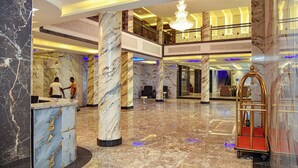 A lobby with marble columns, a reception desk, a gold luggage cart, and a chandelier.