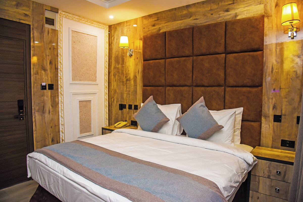 A hotel room with a large bed, wooden headboard, two bedside lamps, and a telephone on the nightstand.