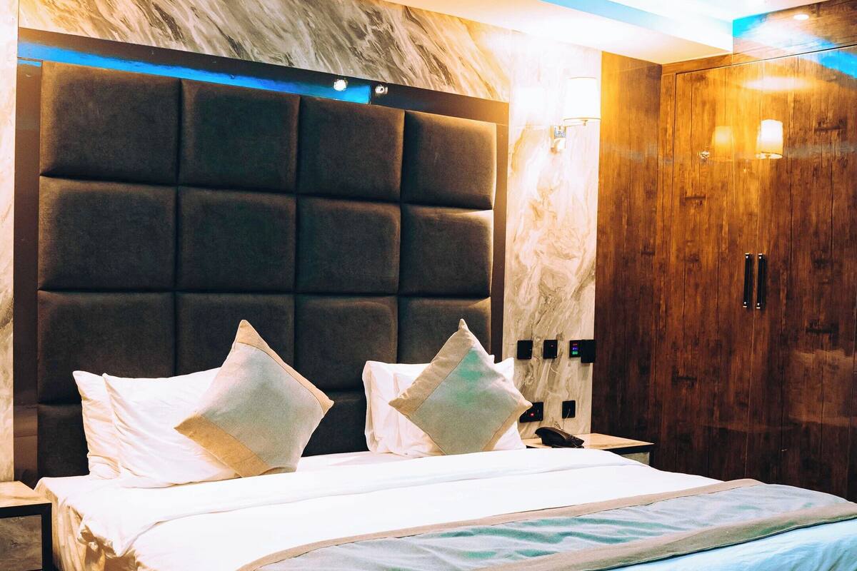 A modern hotel room with a large bed, a wooden wardrobe, and a marble headboard.