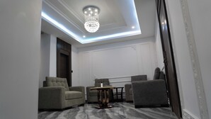 A modern living room with a marble floor, a chandelier, and grey upholstered chairs.