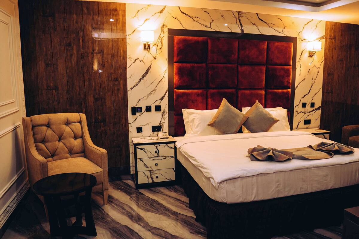 A hotel room with a large bed, a wooden accent wall, marble-patterned walls, and a tufted armchair.