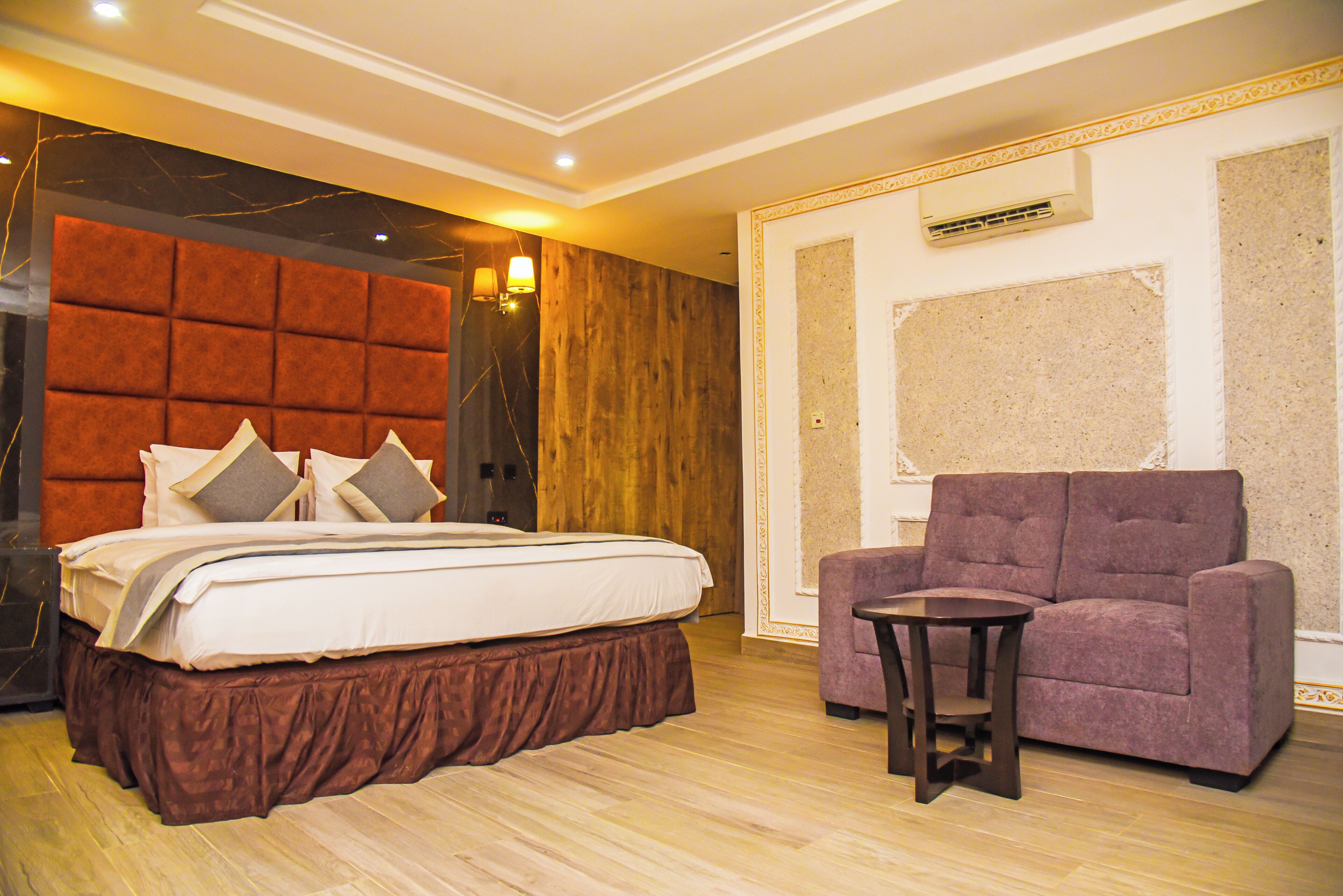 A bedroom with a large bed, a wooden headboard, a purple sofa, and a small table.