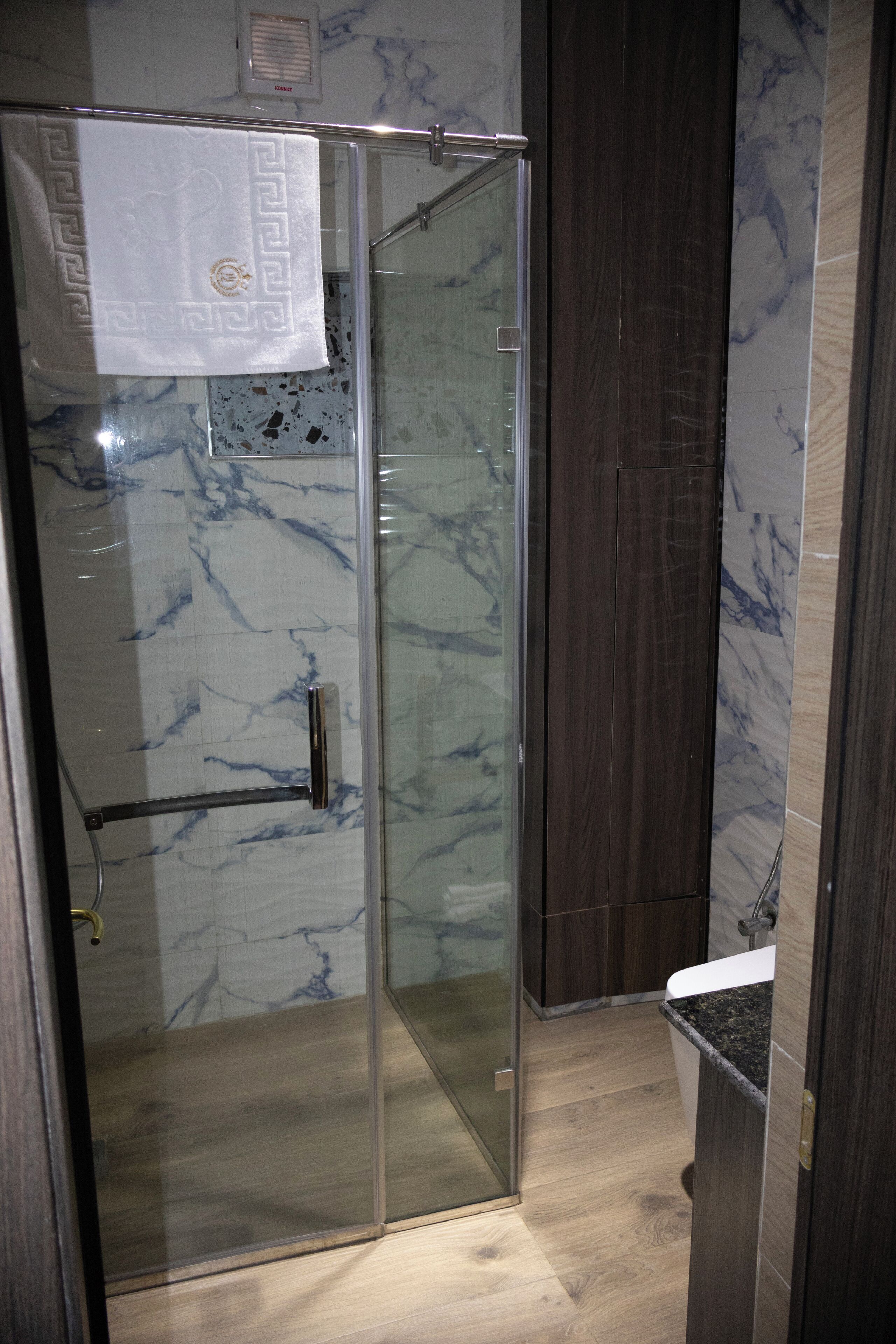 A glass-enclosed shower with a marble wall and a wooden door.