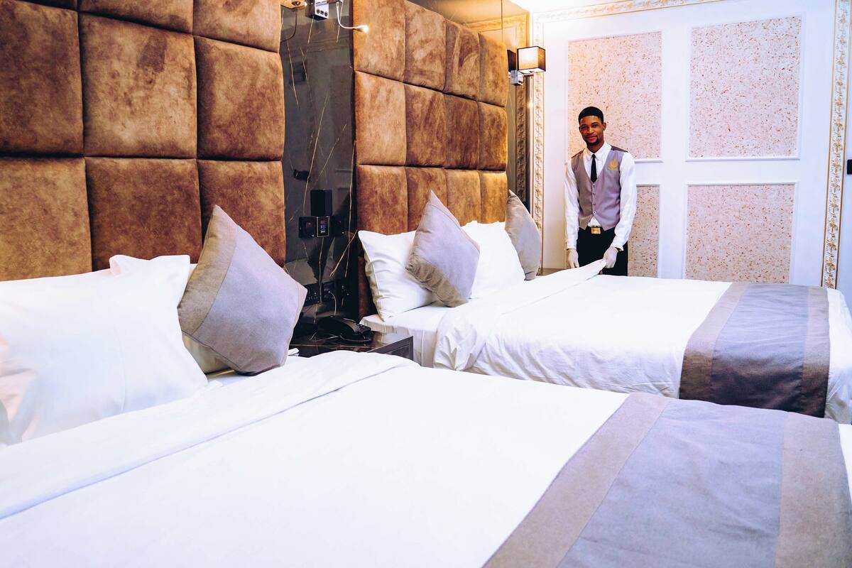 A hotel room with two beds, a large padded headboard, and a modern design.