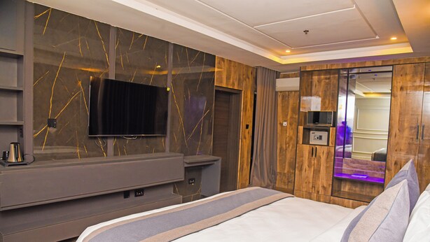 A modern hotel room with a large bed, a flat-screen TV mounted on the wall, and a wooden wardrobe.