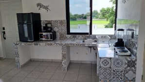 Cocina compacta con refrigerador, microondas, cafetera, lavamanos y licuadora.