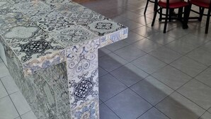 Un cuarto amplio con una isla grande de azulejos, una mesa de comedor con sillas, una escalera y una planta en maceta.