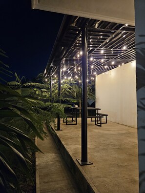 Un patio al aire libre con piso de concreto, columnas de metal negro y mesas y sillas.