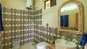 A bathroom with patterned tiles, a toilet, a sink, a mirror, and a shower.