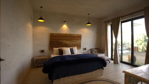 A bedroom with a large bed, bedside tables, a wooden headboard, and a view through a glass door to an outdoor area.