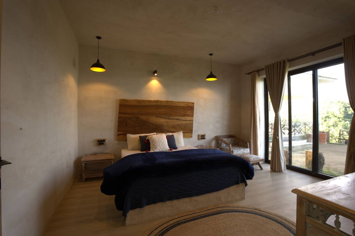 A bedroom with a large bed, bedside tables, a wooden headboard, and a view through a glass door to an outdoor area.