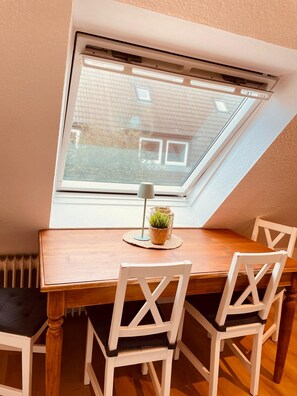 A dining area with a table and chairs, a skylight window, and a view of a building outside.