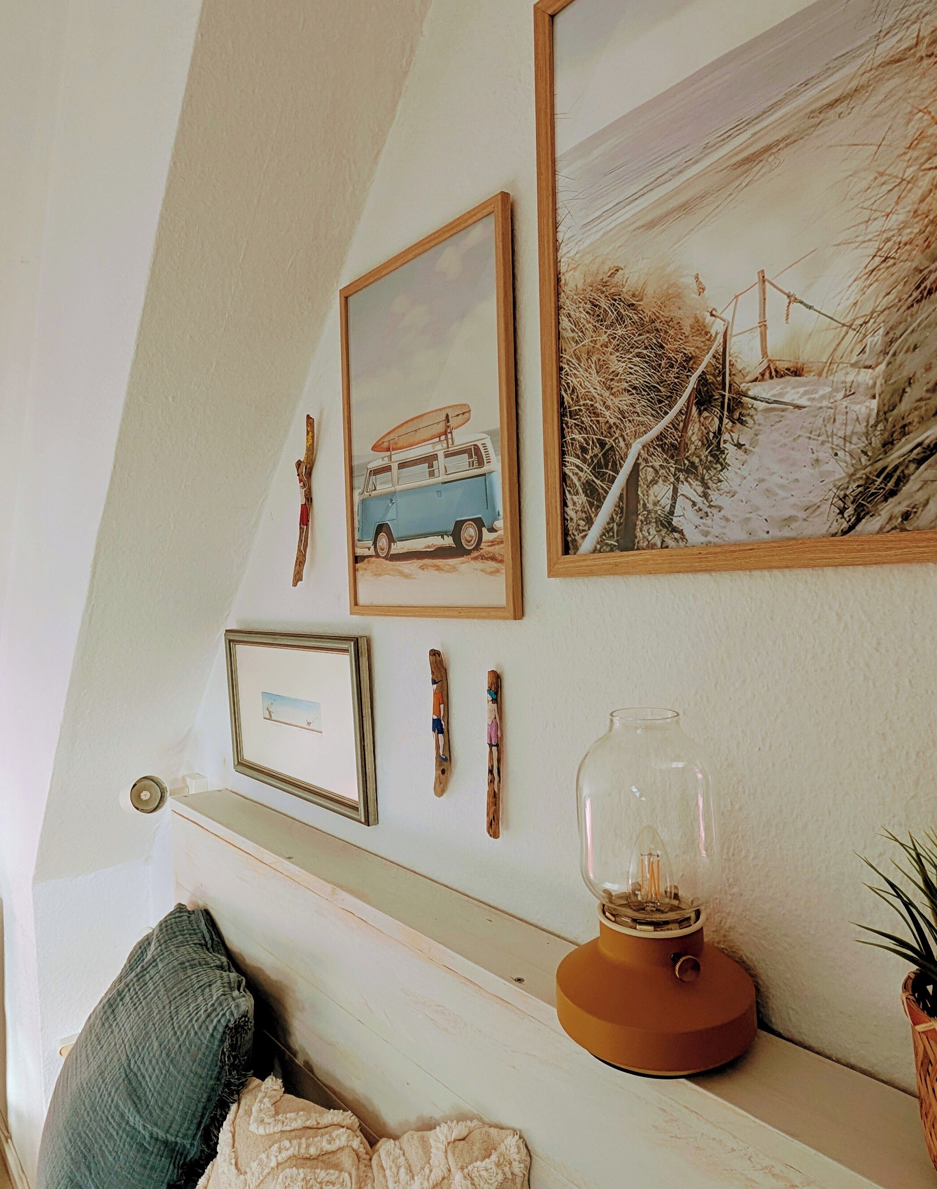 A room with a sloped ceiling, a wooden shelf with various items, a framed picture of a van, and a lamp.