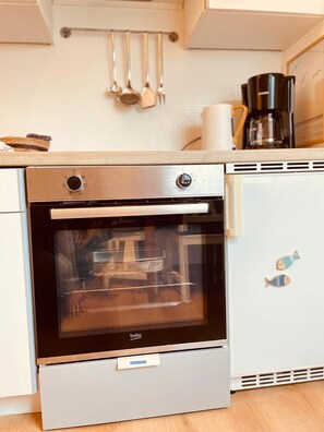 Une cuisine équipée d’un four encastré, d’une machine à café et d’un réfrigérateur décoré d’aimants en forme de poissons.
