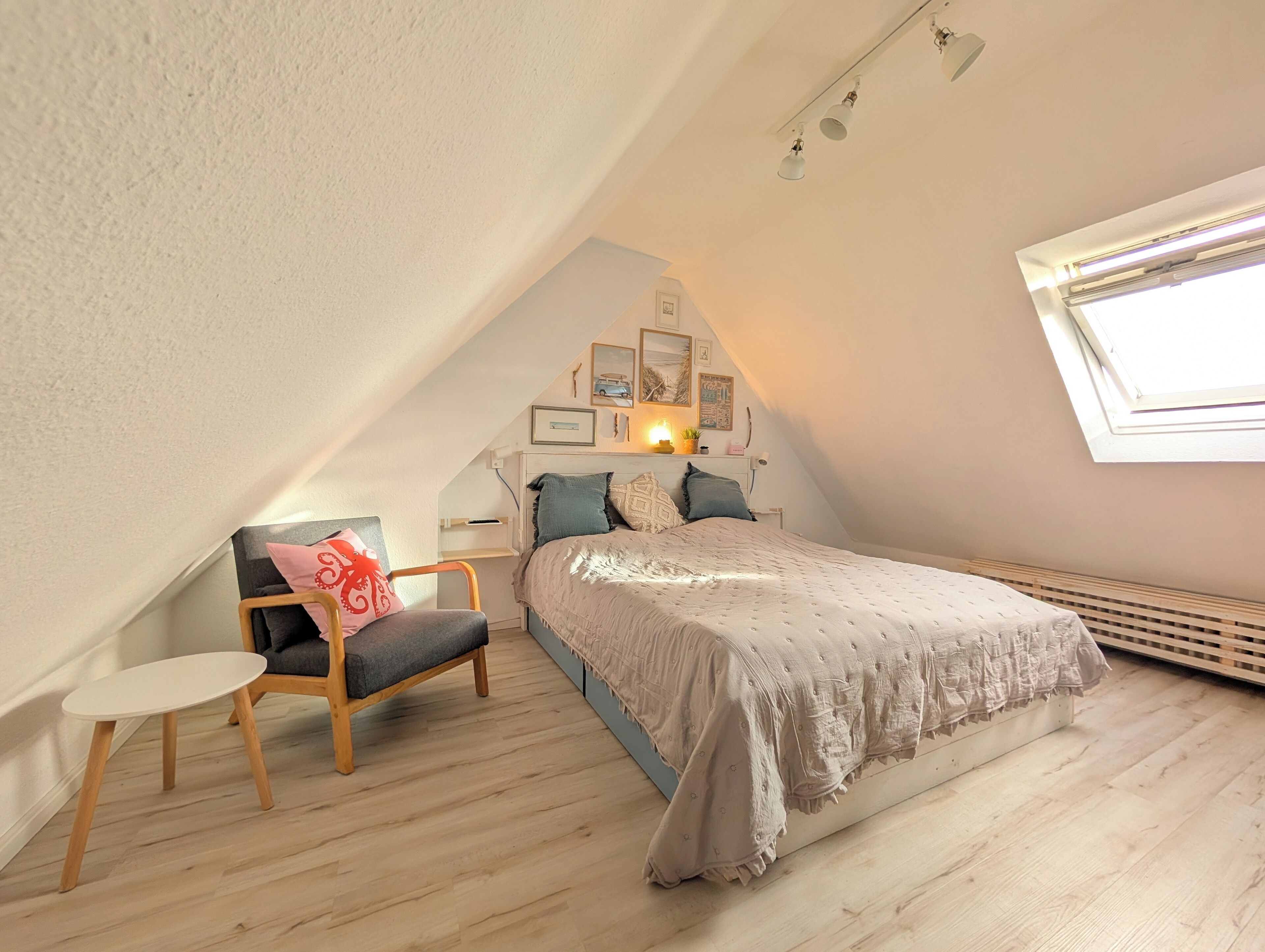 A cozy attic bedroom with a sloped ceiling, a bed with a patterned bedspread, a small round table, and a chair.