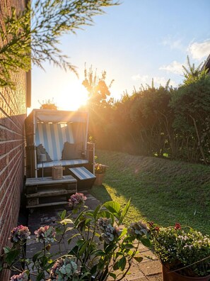 Een terras met een gestreept ligbed, een bijzettafeltje en plantenpotten.