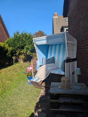 A small outdoor seating area with a blue and white striped bench, a woven basket, and a lamp on a wooden table.