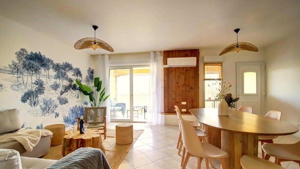 A modern living room with a sofa, coffee table, and dining area with chairs. There is a large window with curtains, a ceiling fan, and a wall-mounted air conditioning unit. - Boheme Piscine Chauffee Privee, 8P - Les Cottages du Tarn (Peyrole)