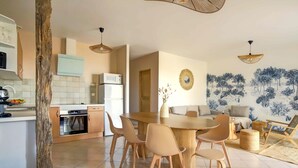 A modern kitchen with white cabinets, a microwave, and a dishwasher. There is a dining area with a round table and chairs, and a living room with a sofa and a coffee table. - Boheme Piscine Chauffee Privee, 8P - Les Cottages du Tarn (Peyrole)