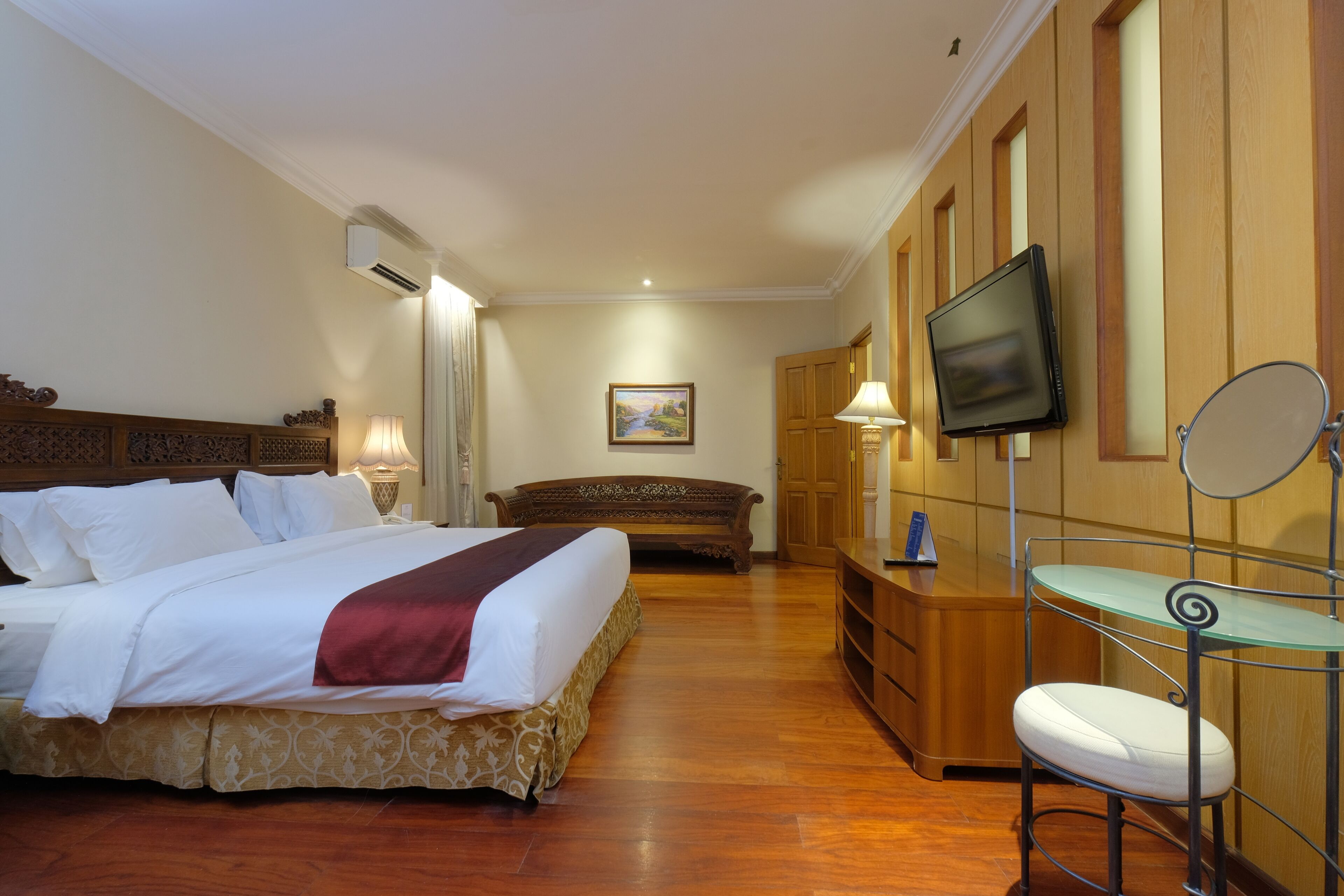 A hotel room with a bed, a desk, a chair, a television, and a painting on the wall.