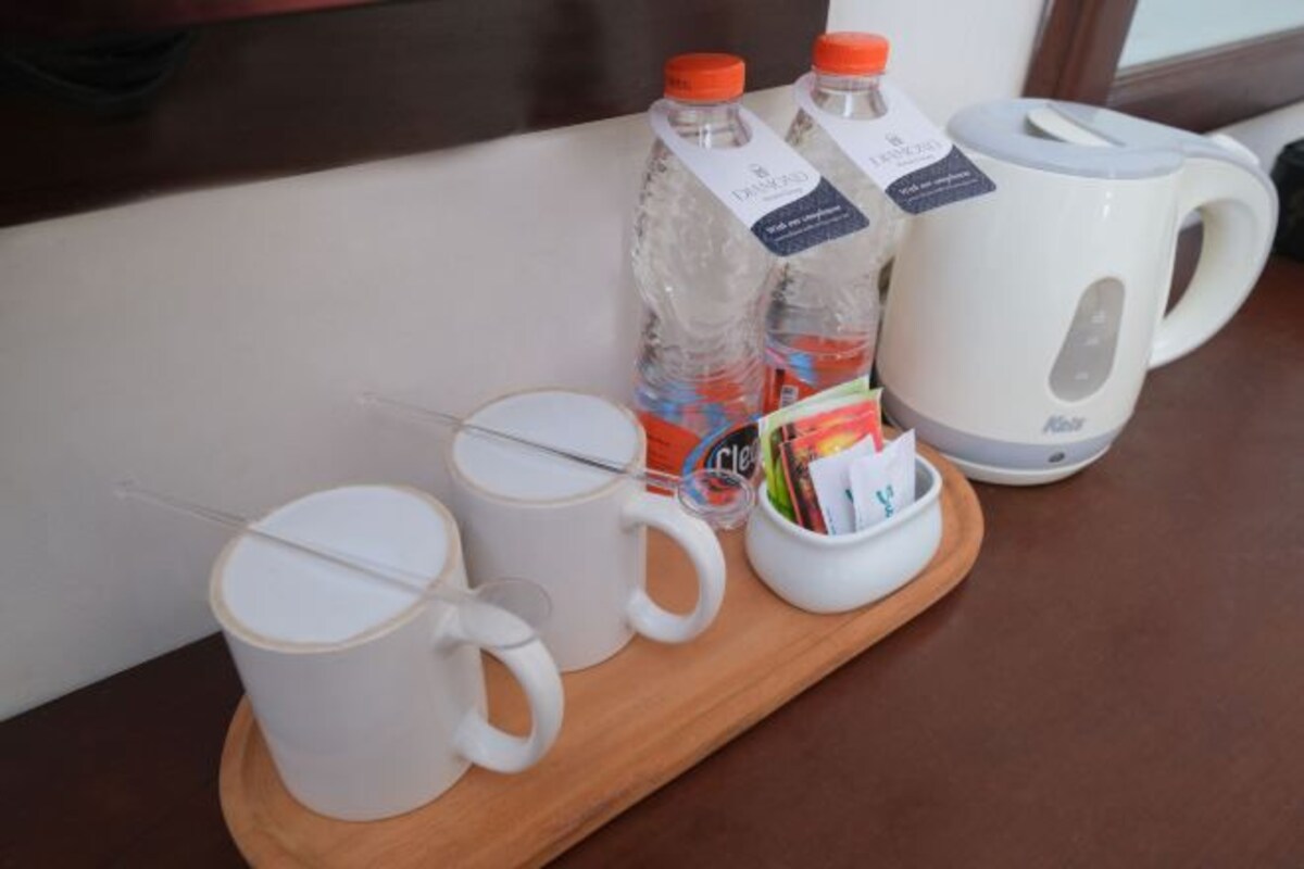 A tray with two white mugs, two bottles of water, a white electric kettle, and a small white cup with a spoon.