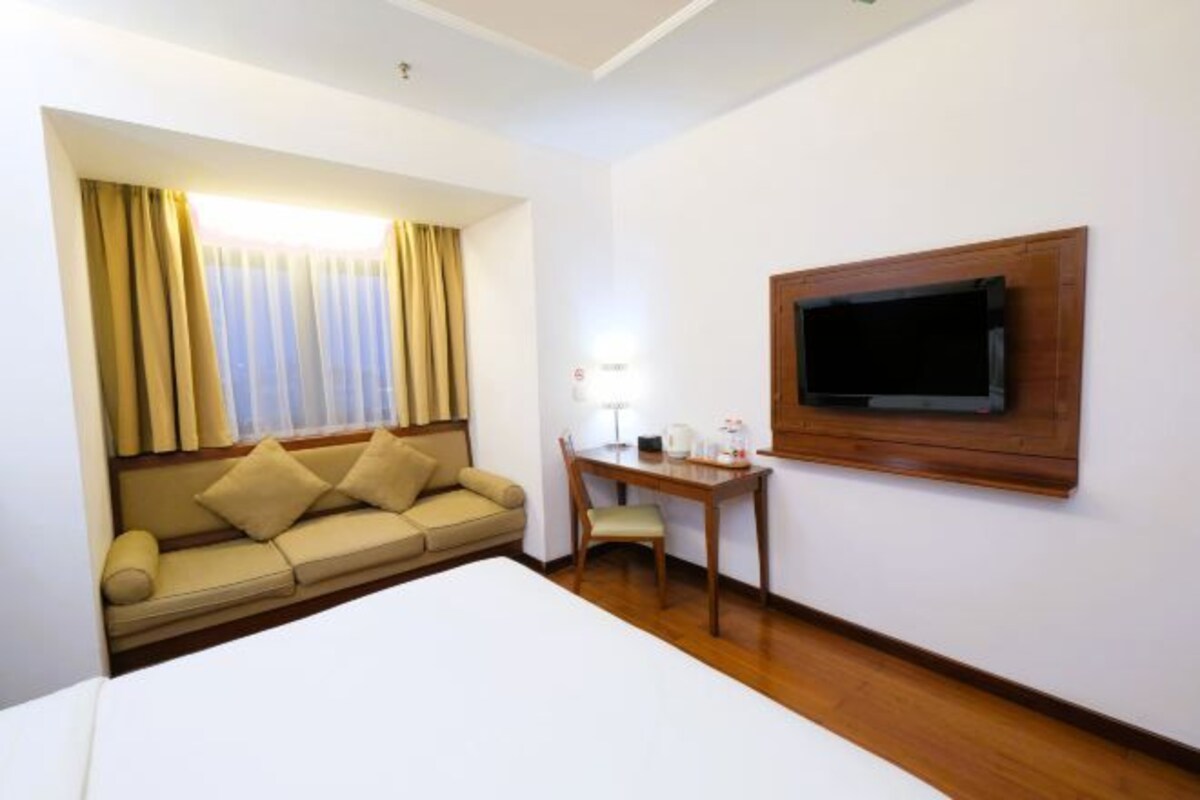 A hotel room with a bed, a sofa, a desk, and a TV mounted on the wall.
