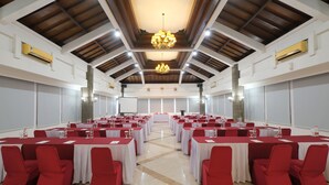 Un salón de conferencias con varias mesas y sillas, una araña y paredes blancas con vigas de madera.