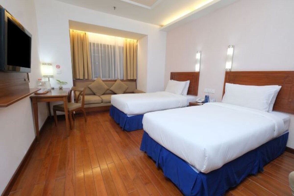 A hotel room with two beds, a desk, a TV, and a window with curtains.