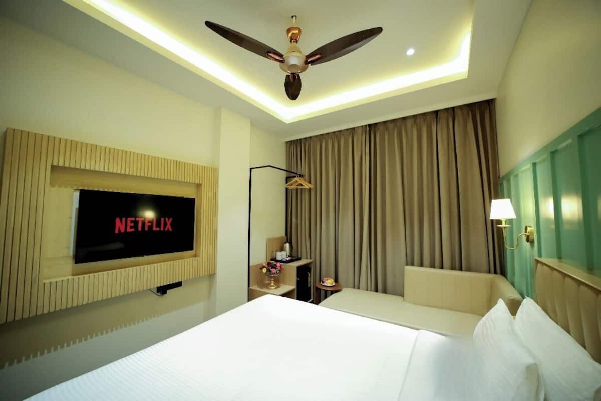 A hotel room with a bed, a TV mounted on the wall displaying 'NETFLIX', a ceiling fan, and a window with curtains.