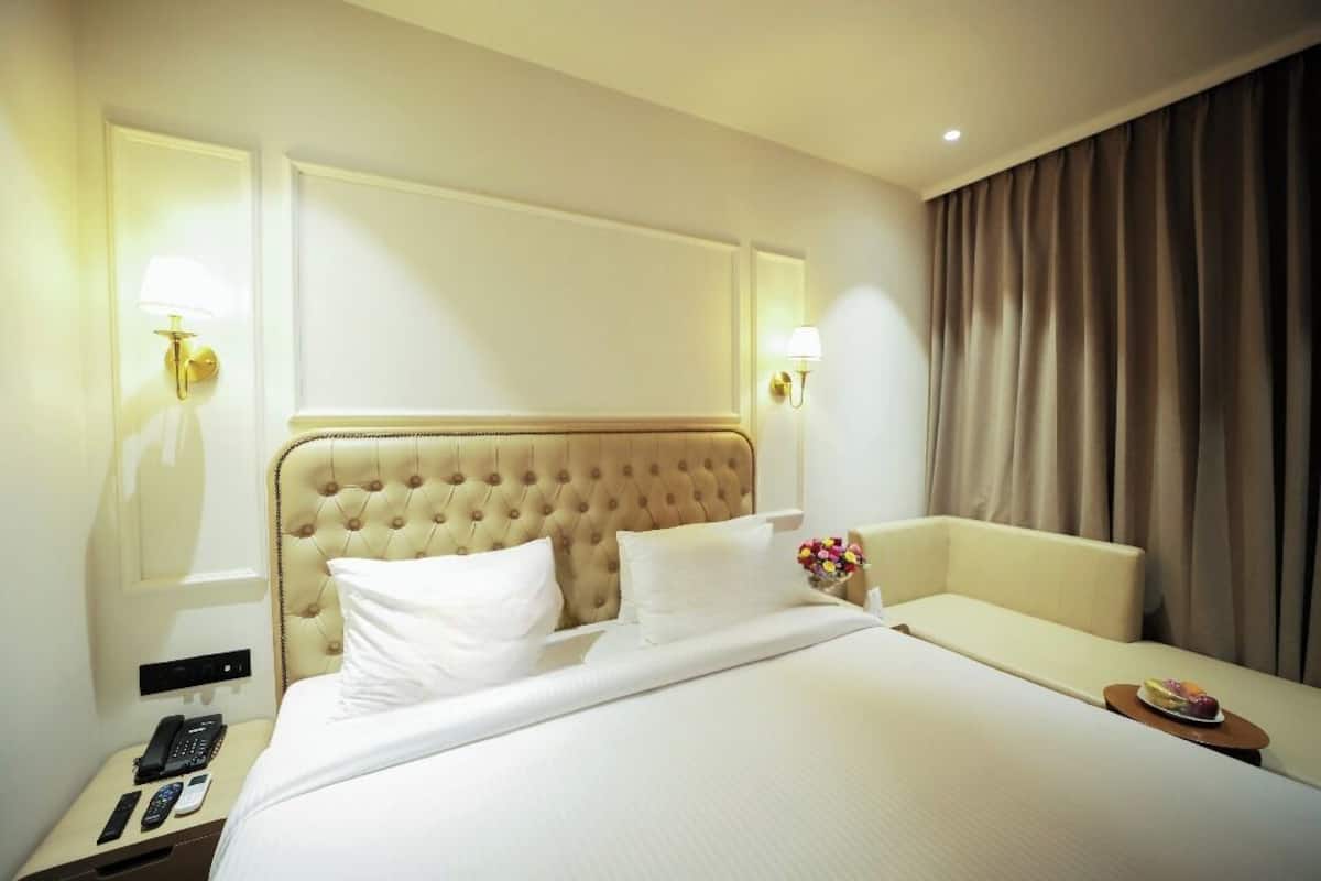 A hotel room with a large bed, a bedside table with a phone and remote controls, and a small table with a plate of fruit.