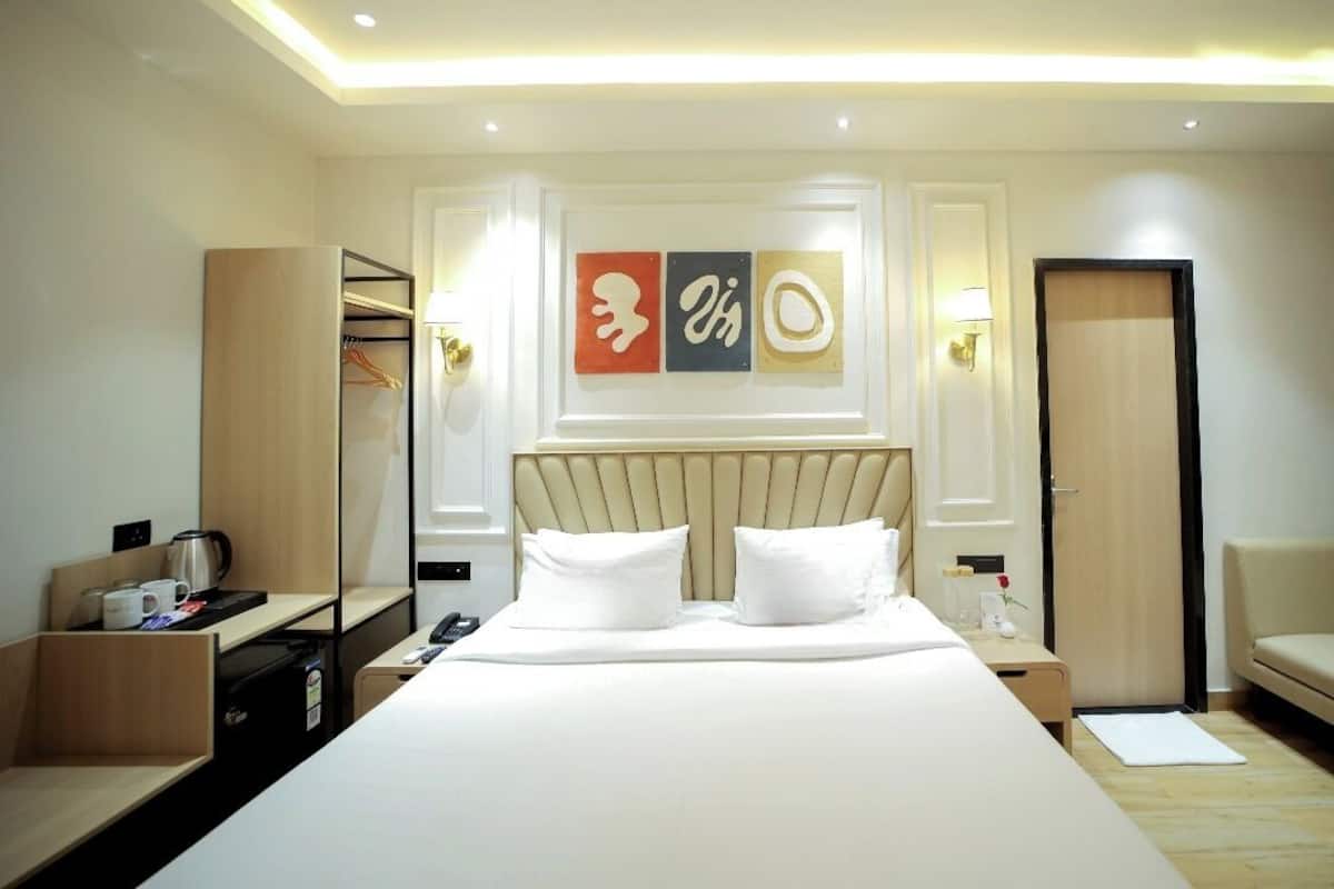 A hotel room with a large bed, a bedside table with a lamp, a wardrobe, and a wall with abstract art.