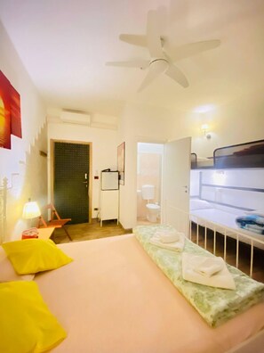 A hotel room with a bed, a ceiling fan, a desk with a lamp, a bathroom, and a small kitchenette. - Europe station rooms (Parma)