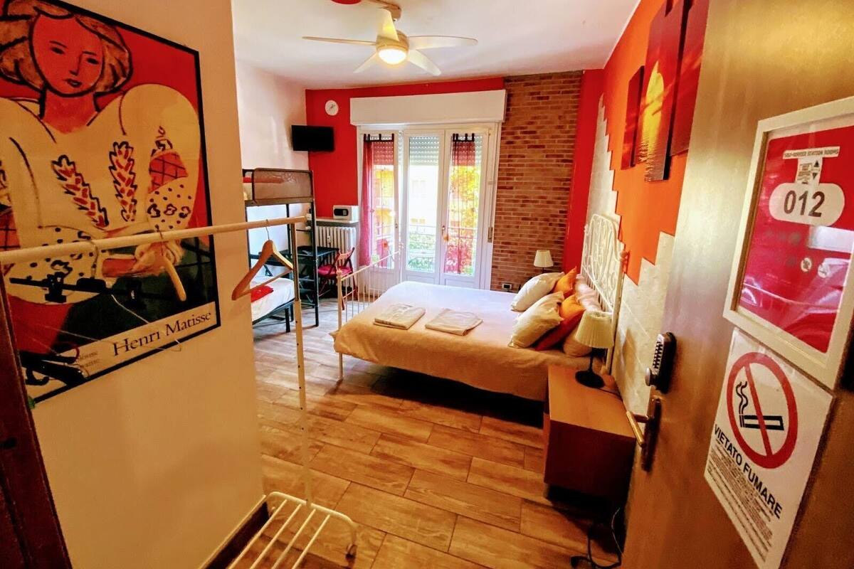 A bedroom with a bed, a radiator, a ceiling fan, a window with a view, and a door leading to another room.