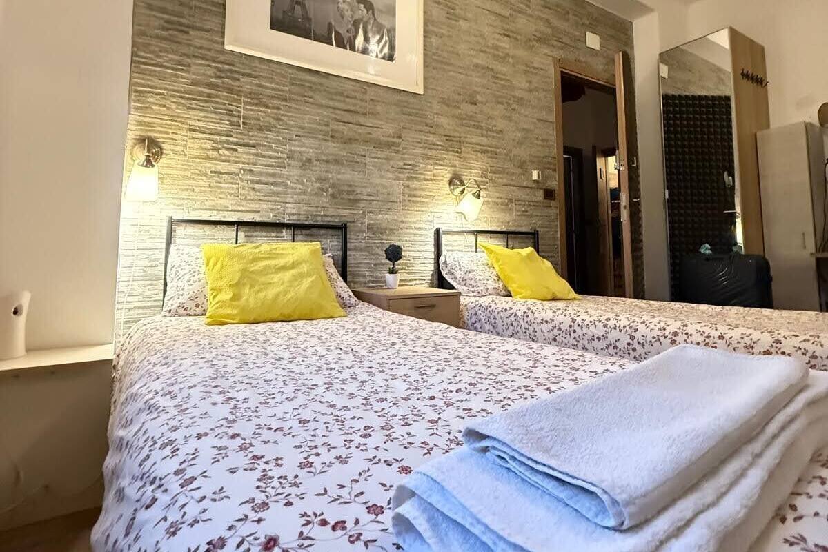 A bedroom with two beds, a wooden accent wall, a framed picture, bedside lamps, and a mirror.