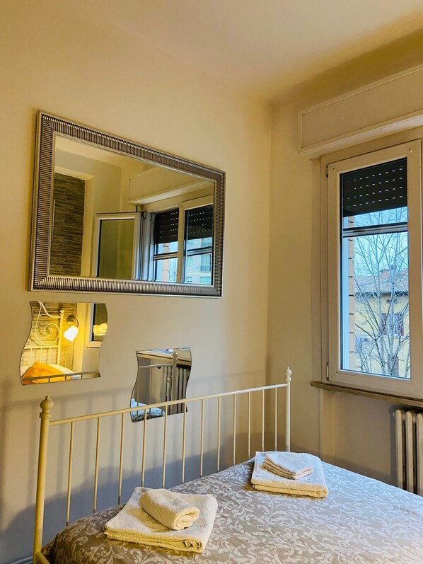Habitación de hotel con cama, un espejo grande, un radiador y ventana con vista a edificios.